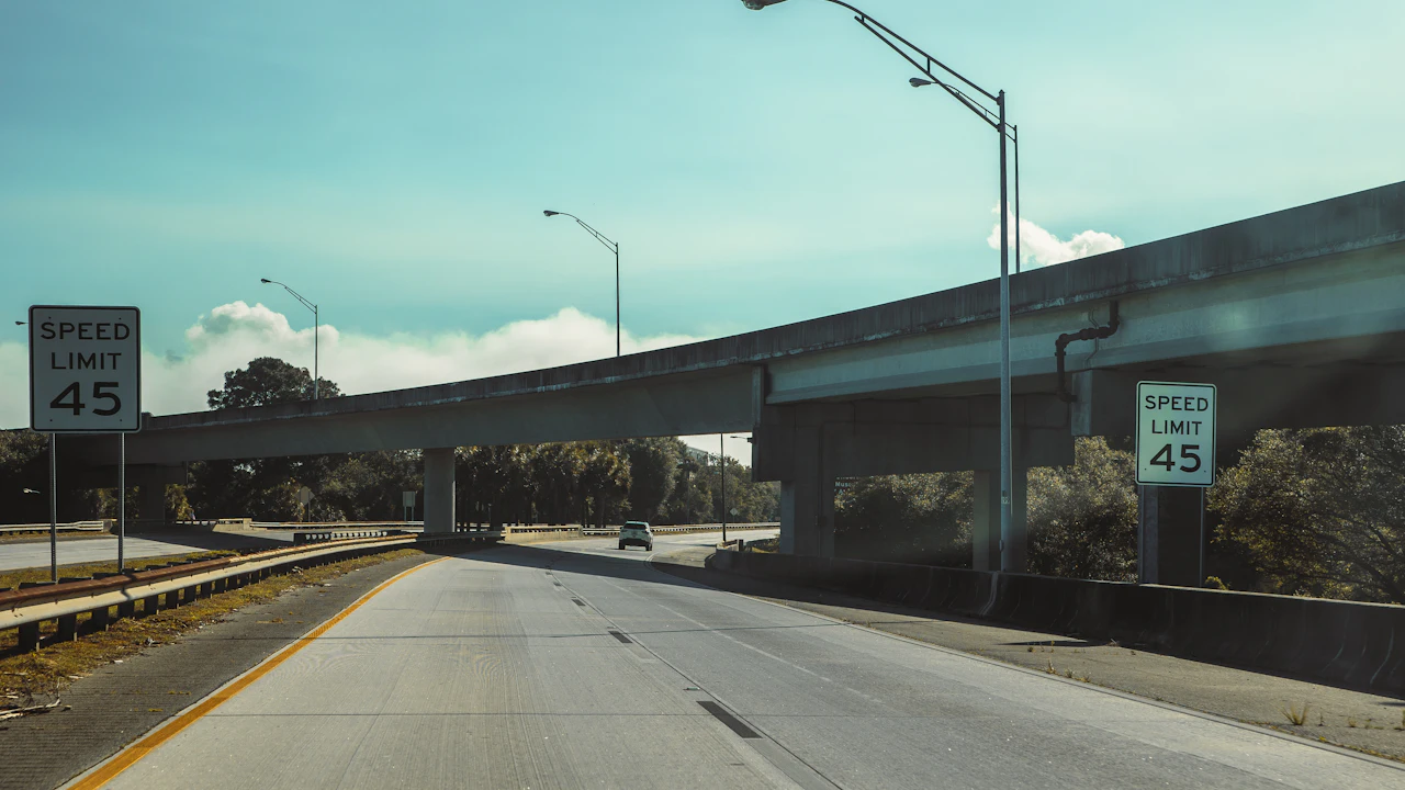 An American freeway passing beneath a concrete overpass, speed-limit signs on both shoulders