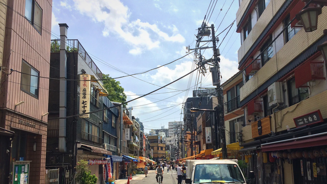 A narrow Tokyo shopping street crowded with low-rise buildings and overhead cables, a white kei truck parked among pedestrians