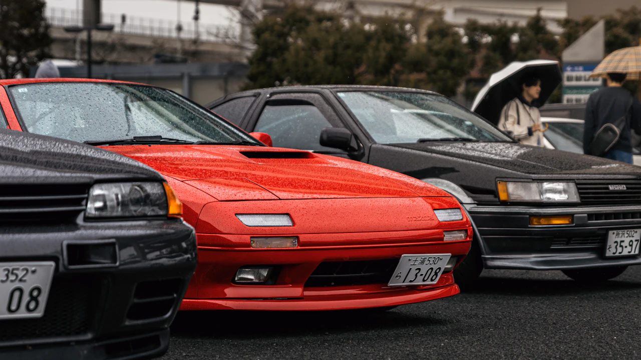 Three Japanese sports coupes from the late eighties nose-in at a rainy car meet, home-market plates still fitted