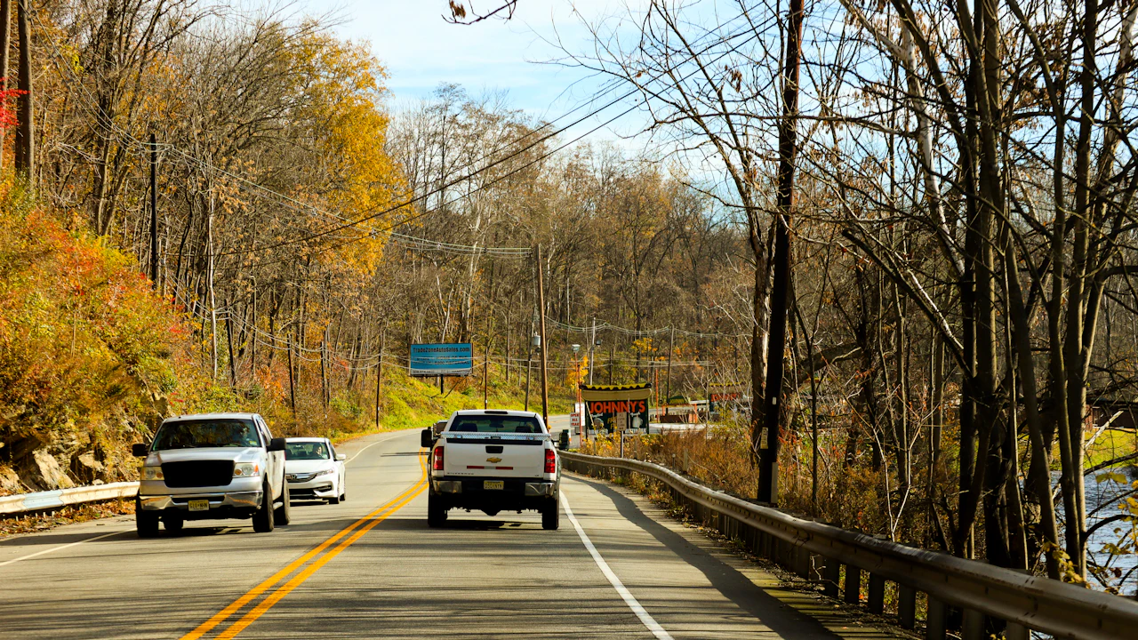 Pickup trucks on a two-lane road lined with autumn trees, a guardrail along the shoulder