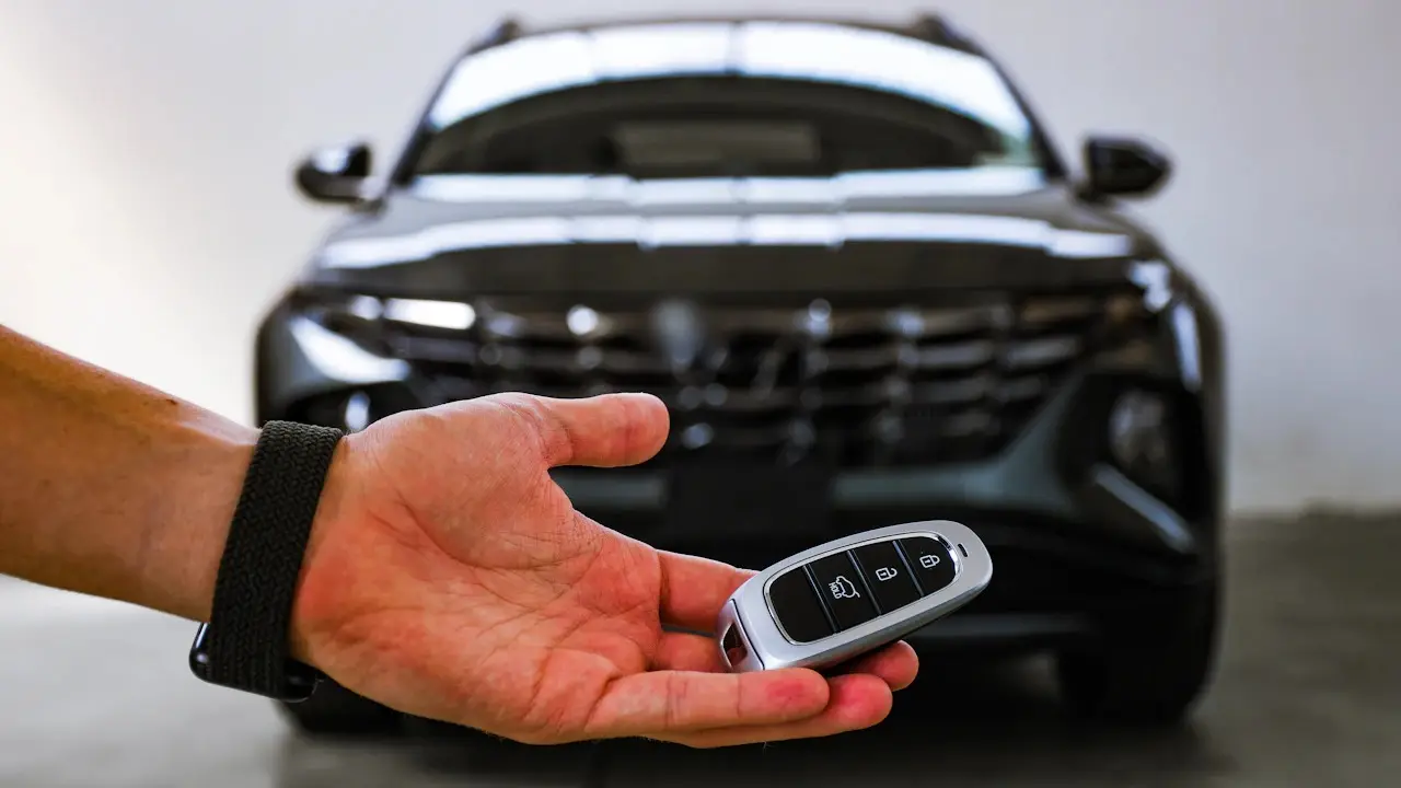 A hand holding out a car's keyless remote in front of a dark SUV.