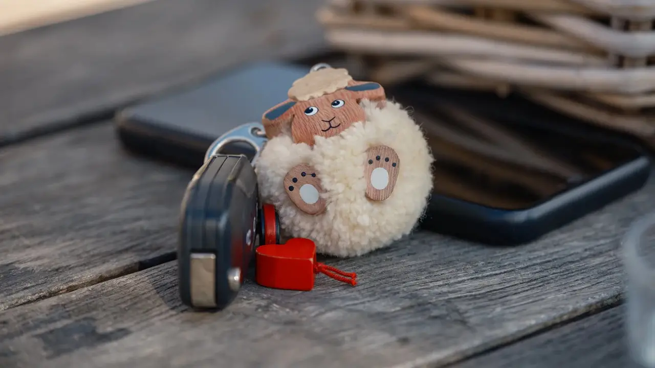 A car key fob and a phone on a wooden table beside a fluffy sheep keyring.