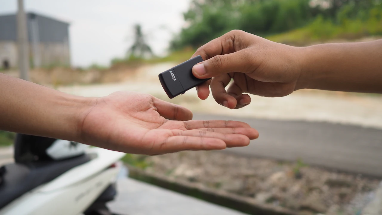 One person passing a black key fob into another person's open palm outdoors