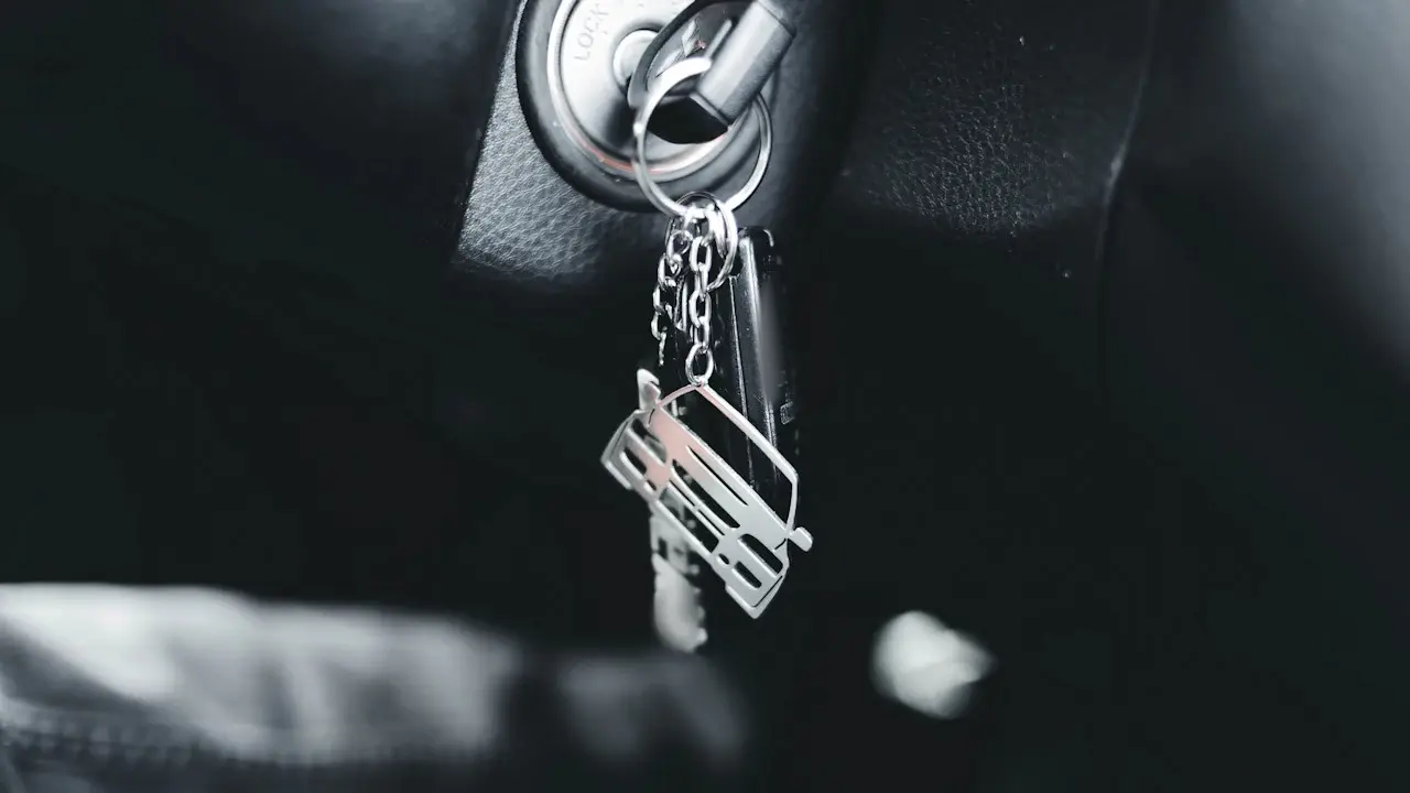 A car key with a metal keyring charm hanging from an ignition lock.