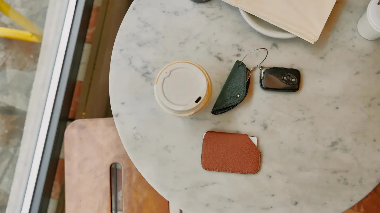 A car's smart key, a leather key pouch, a card wallet and a coffee cup on a marble table, seen from above.