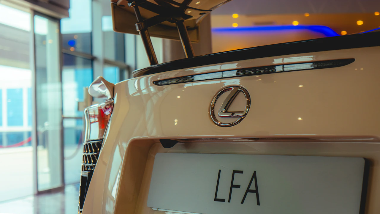 The rear deck of a white Lexus LFA in a showroom, the oval badge above an LFA plate, a rear wing overhead