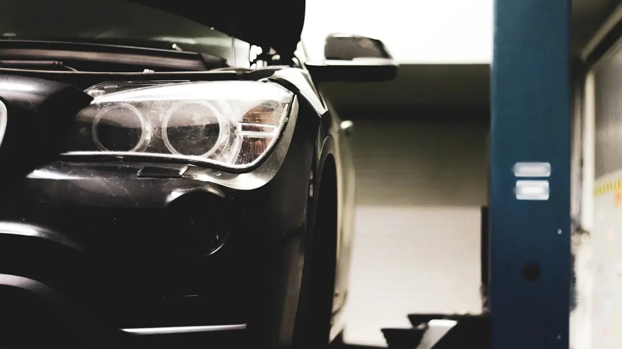 A dark car's headlamp and front end beside a workshop lift post.