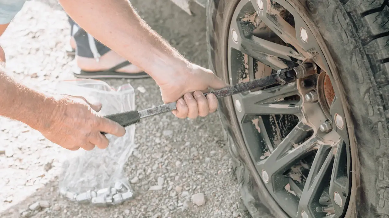 Hands using a lug wrench on a flat tire's wheel.