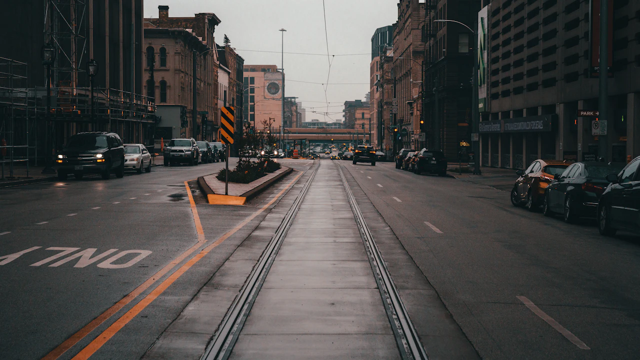 A wet Milwaukee street at dusk with streetcar tracks down the centre and cars parked along both kerbs