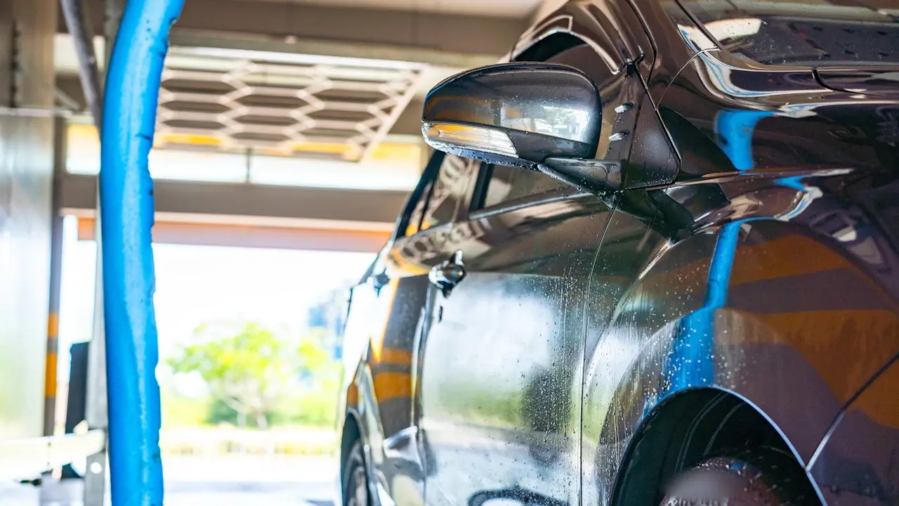 A car’s side mirror passing a wash brush in an automatic car wash.