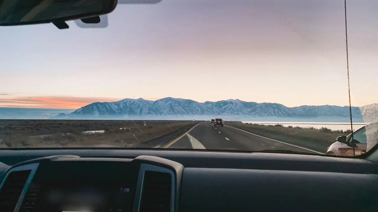 The road ahead through a car's windscreen at dusk, mountains on the horizon, the rear-view mirror at the top.