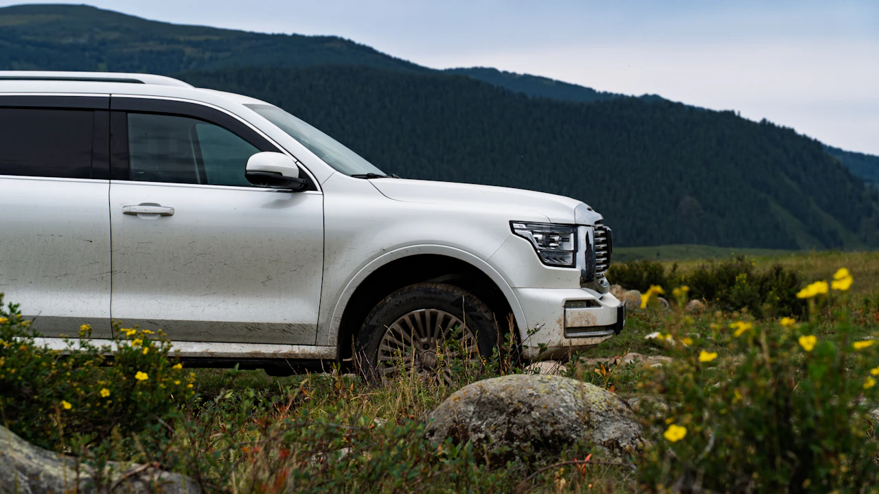 A white SUV parked on a grassy field with mountains in the background