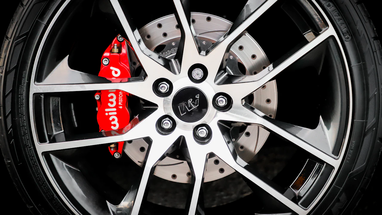 An aftermarket alloy wheel with a red six-piston brake caliper and a cross-drilled disc visible behind the spokes