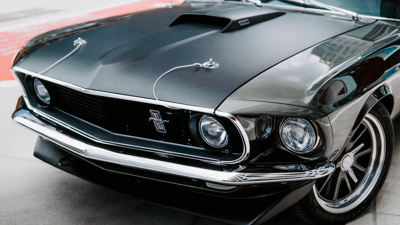 The front of a black nineteen-sixties American muscle car photographed low and close, chrome bumper and quad headlights filling the frame