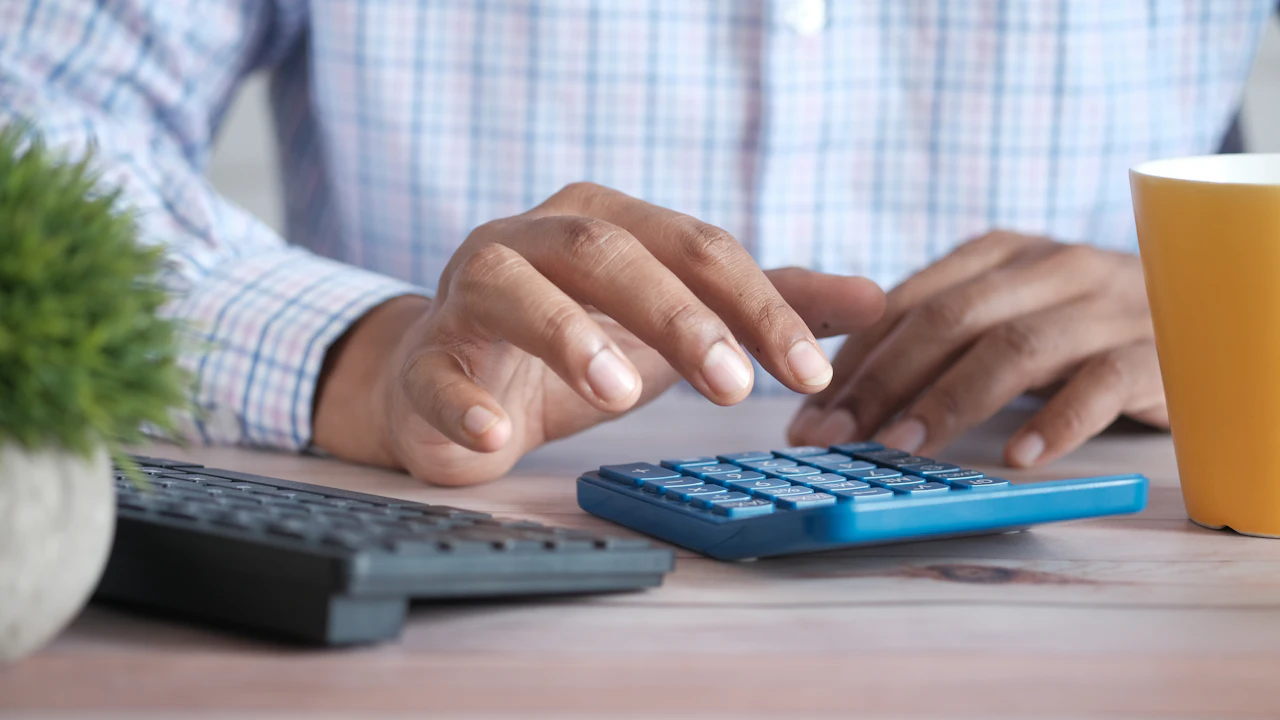 A person working through paperwork with a calculator at a desk