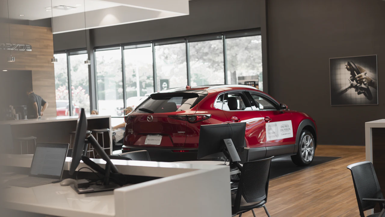 A red compact SUV parked inside a dealership showroom beside sales desks with computer monitors