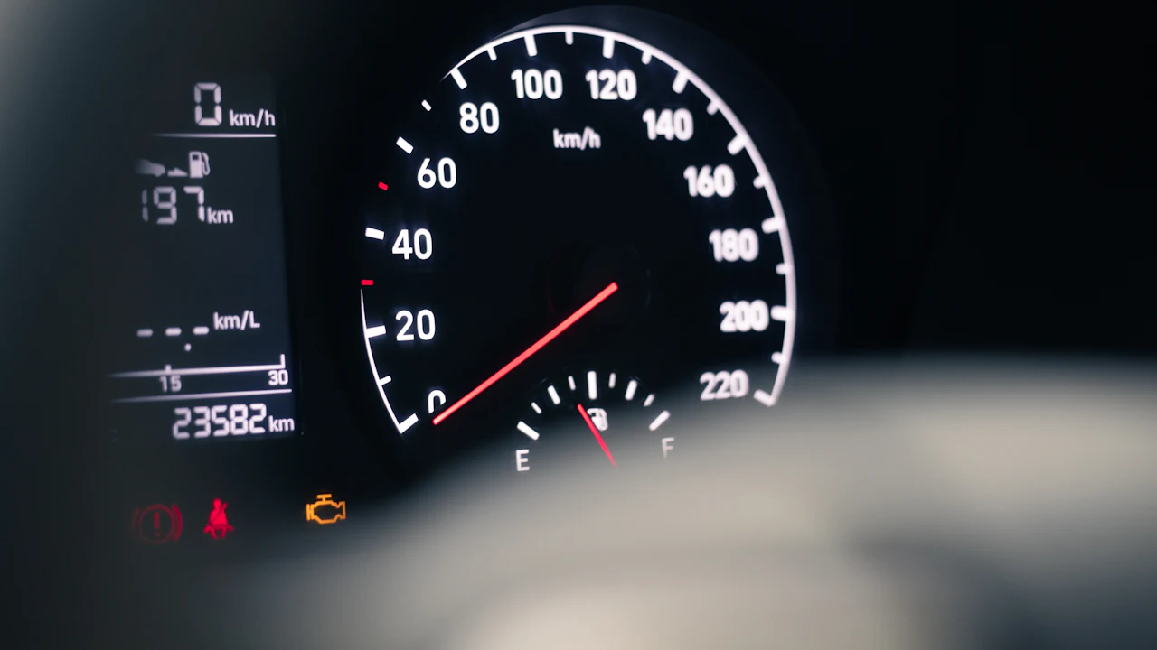 A car's instrument cluster: the odometer readout, the speedometer and fuel gauge, and a row of warning lights including an amber engine light.