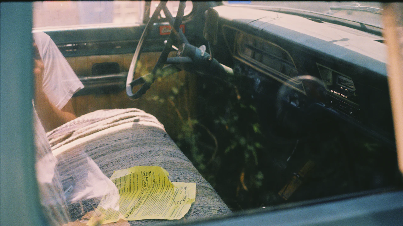 A yellowed document lying on the bench seat of an old truck, photographed through the side window with the steering wheel above it