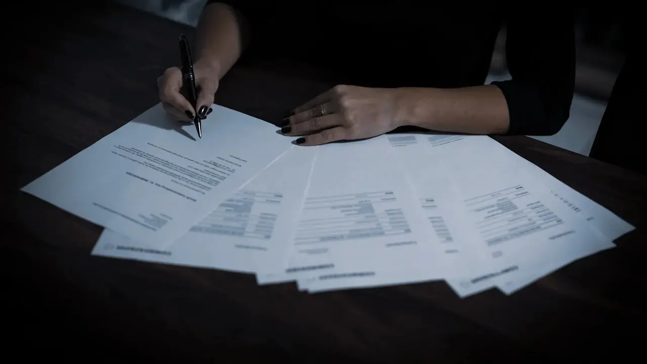 A hand signing one of several loan documents spread on a table.