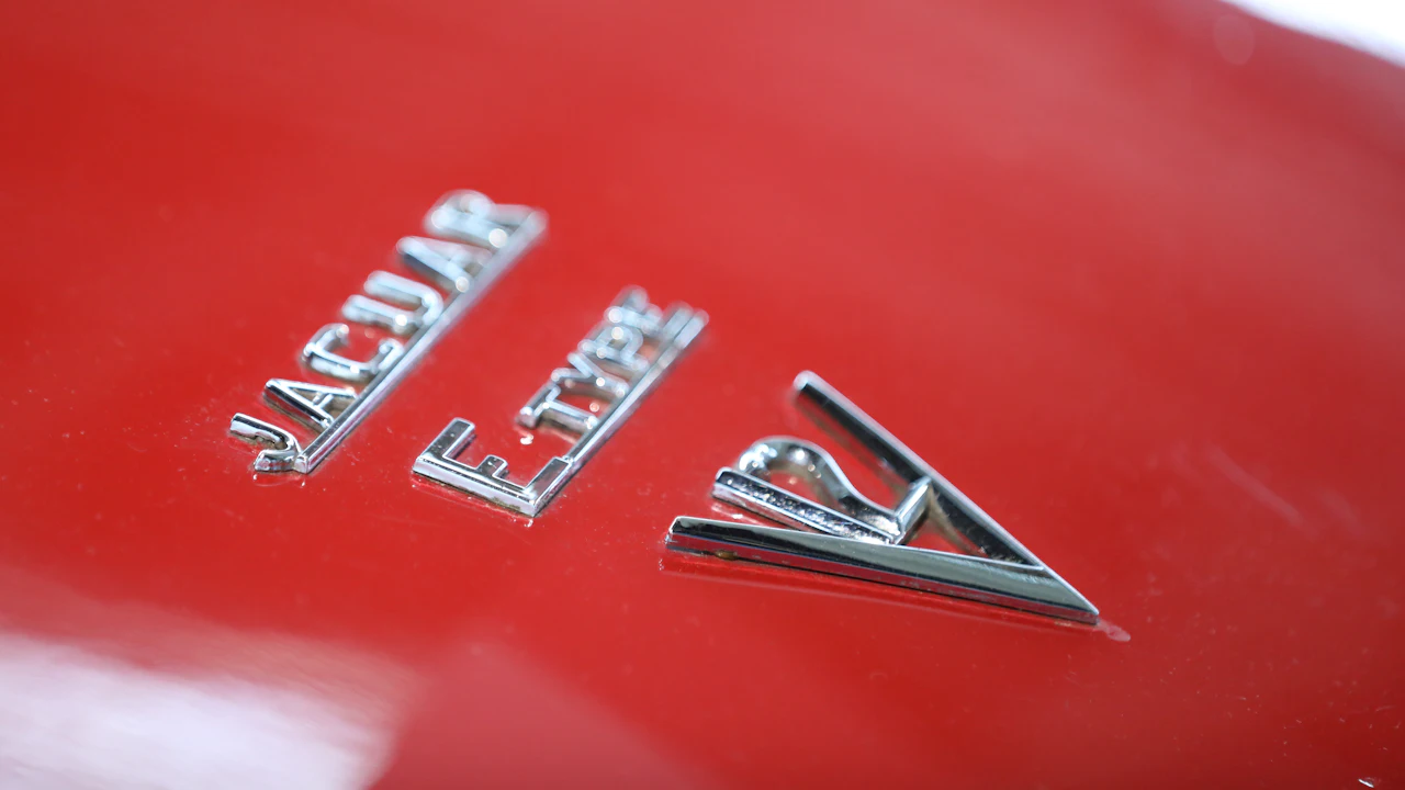 A chrome Jaguar E-Type badge on red bodywork, photographed close up