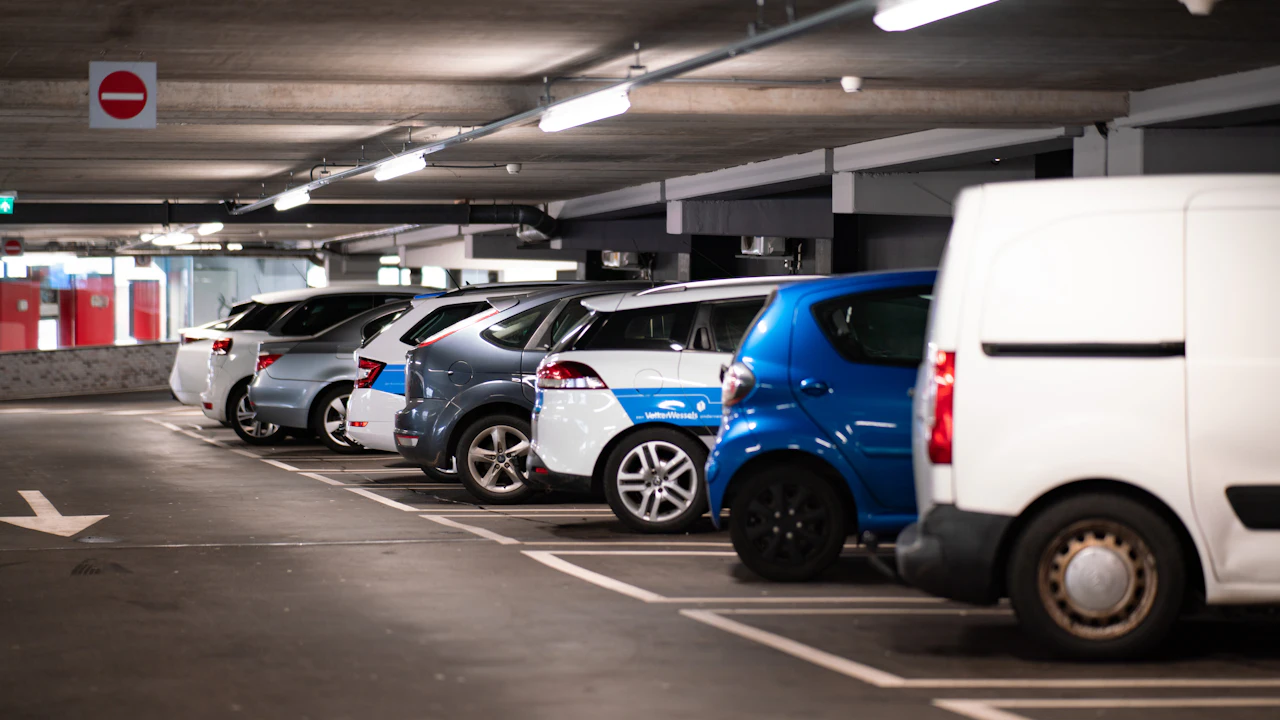 A row of cars parked nose-in on a level of a concrete multi-storey car park, seen from behind under strip lighting