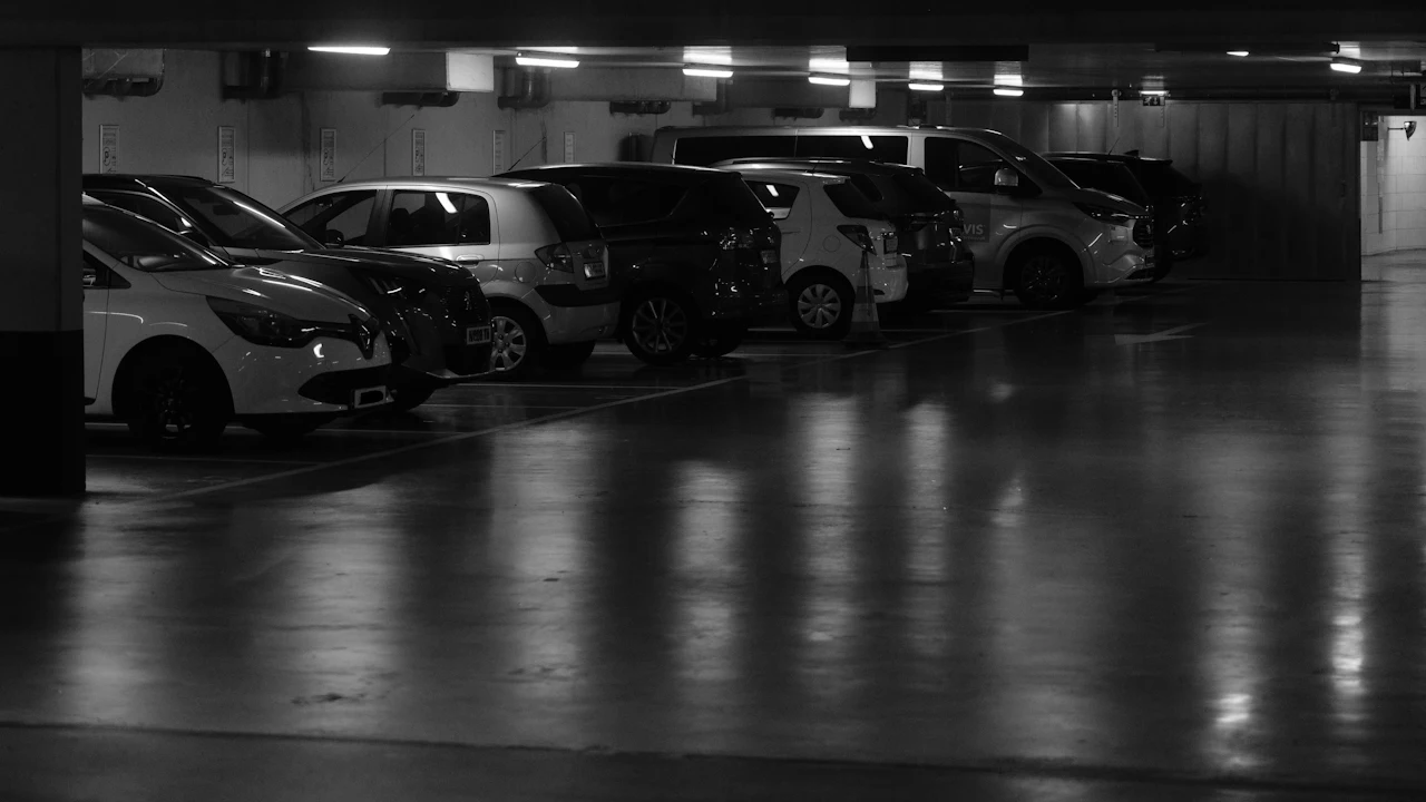 Cars parked nose-in along a dim concrete parking structure, ceiling lights reflecting off the floor