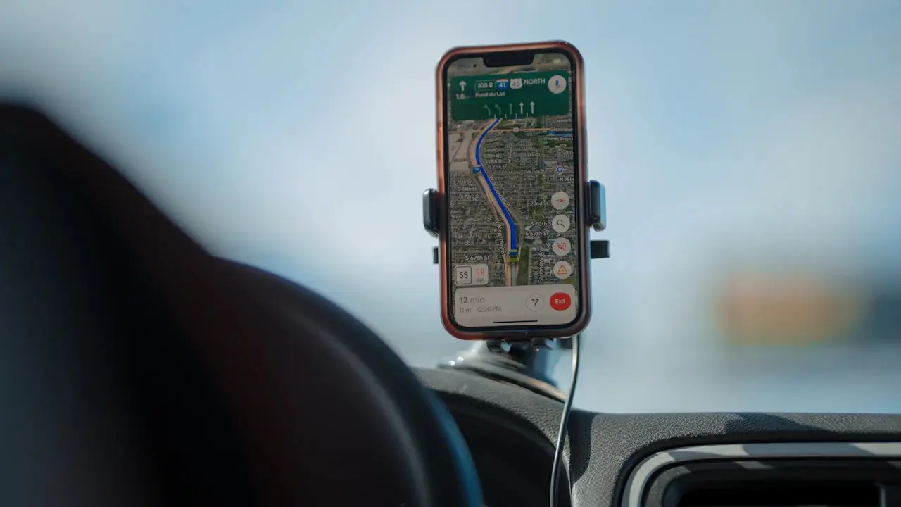 A phone in a dashboard mount showing a navigation map, the steering wheel blurred in the foreground.