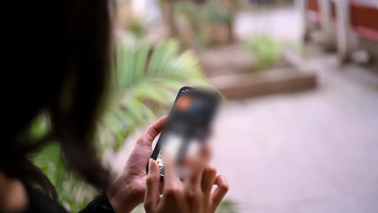 Hands holding a smartphone outdoors.