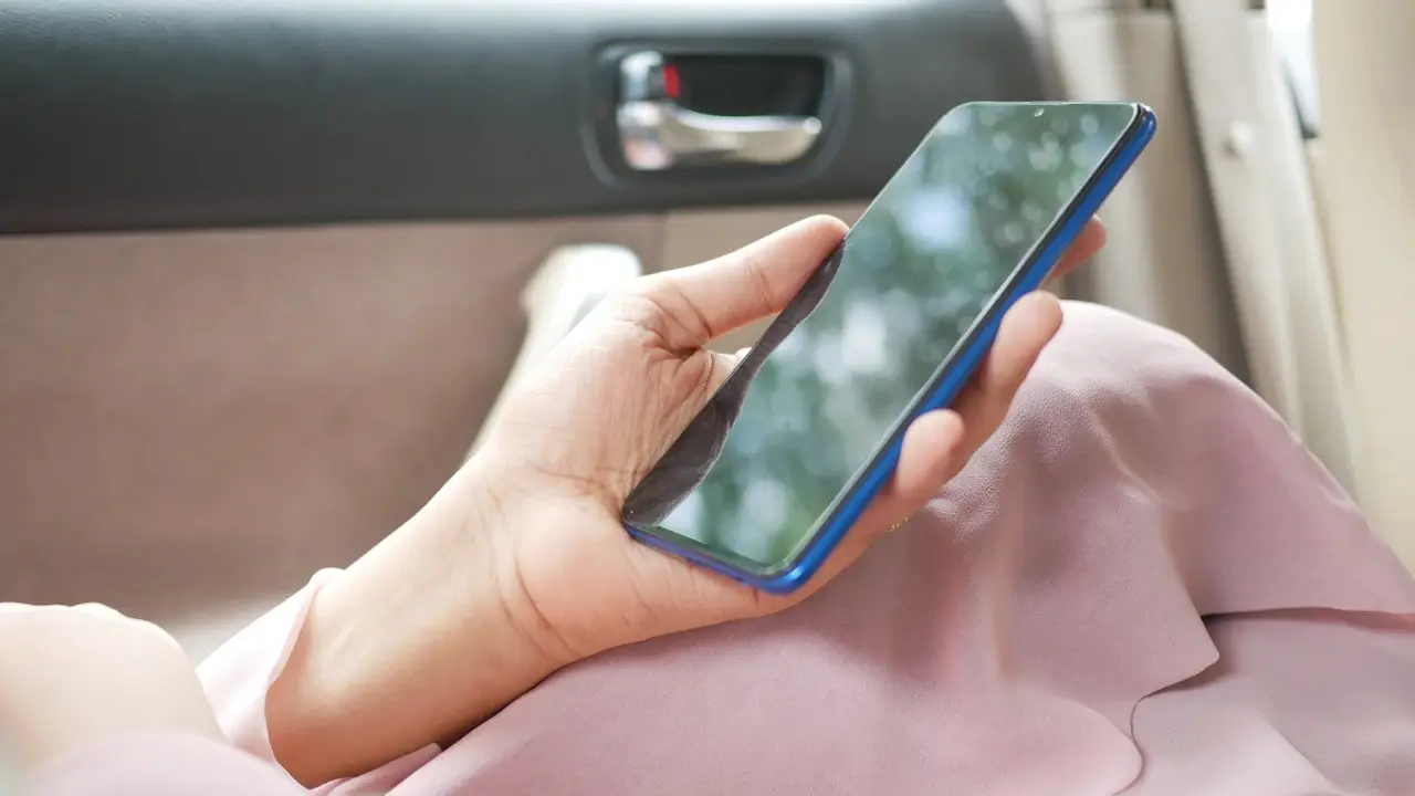 A hand holding a smartphone inside a car.