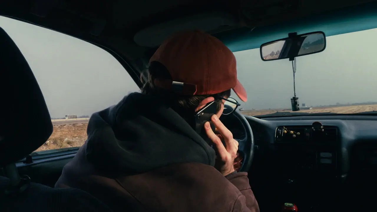 A man in a cap talking on a phone in the driver’s seat of a car.