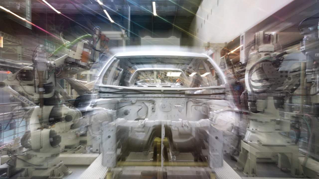 A pickup body shell suspended in a factory cell, welding robots on both sides, motion-blurred sparks and light trails