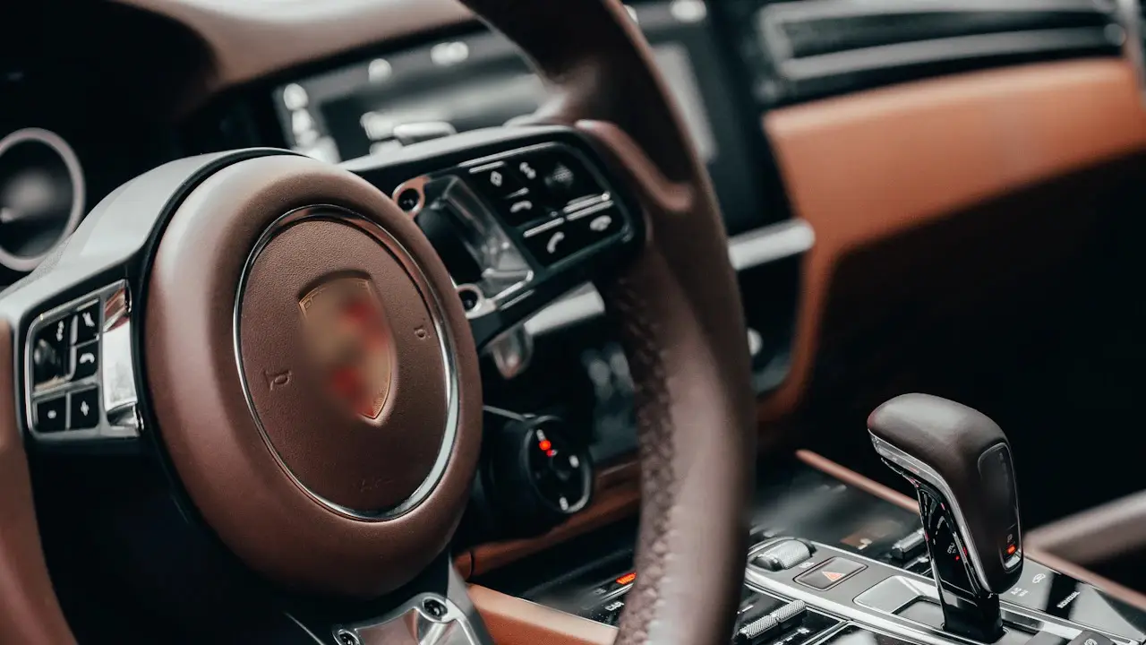 The cockpit of a modern Porsche SUV: steering wheel, instrument cluster and gear selector in brown leather.