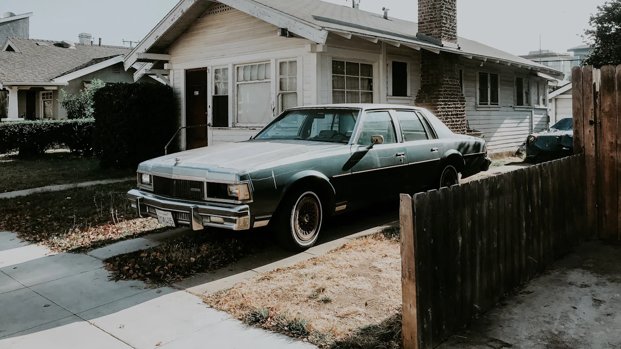 An older two-tone sedan parked on a driveway in front of a house