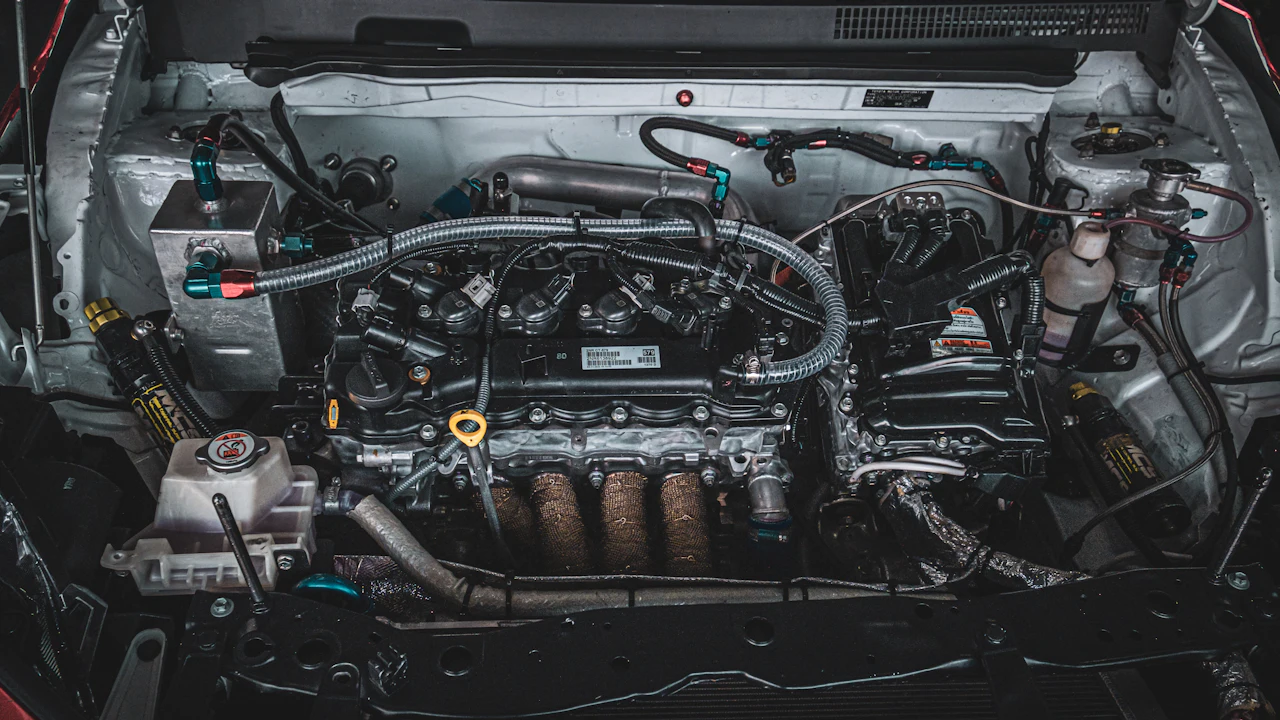 A clean four-cylinder engine bay under an open hood: ignition coils and intake across the top of the engine, a coolant reservoir and brake-fluid reservoir at the sides, wiring and hoses routed across.