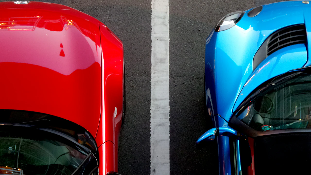 Two cars, one red and one blue, parked nose-first either side of a painted white line