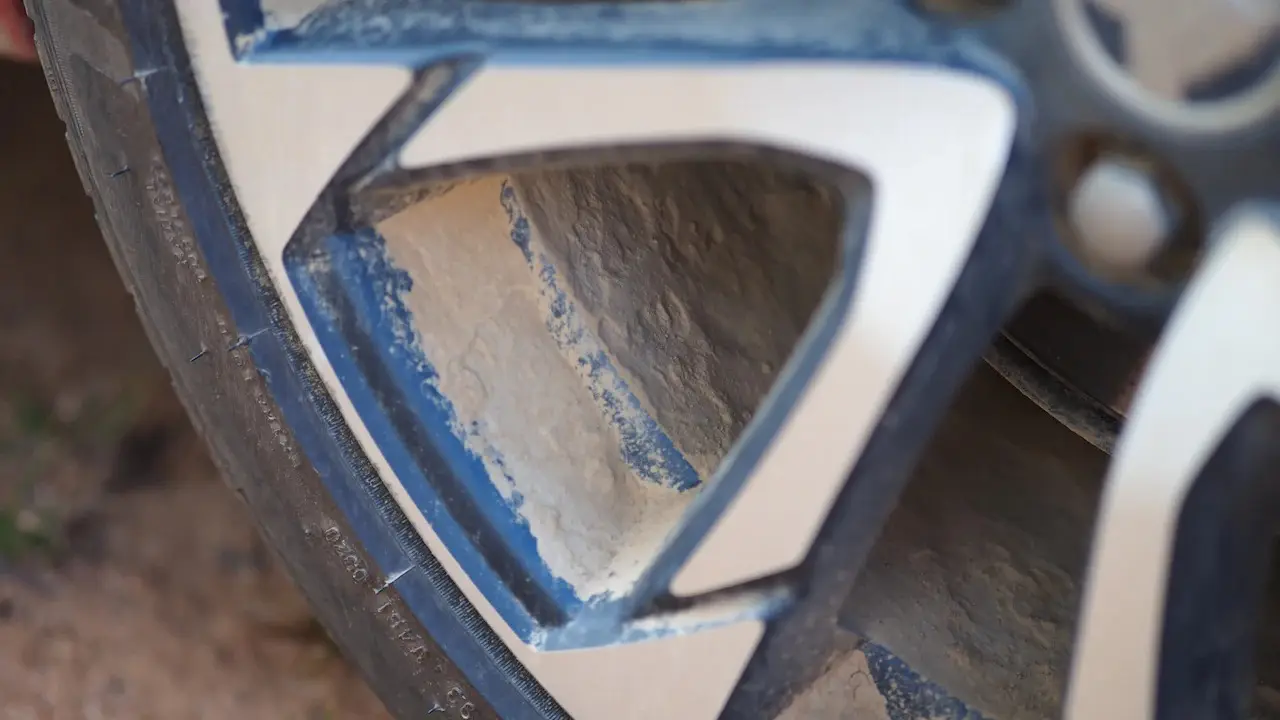 Close view of an alloy wheel spoke with paint scuffs and the tire's sidewall beside it.