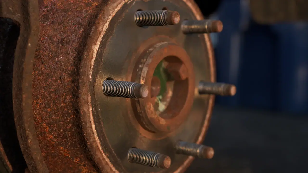 A rusty brake rotor and hub with wheel studs, the wheel removed.