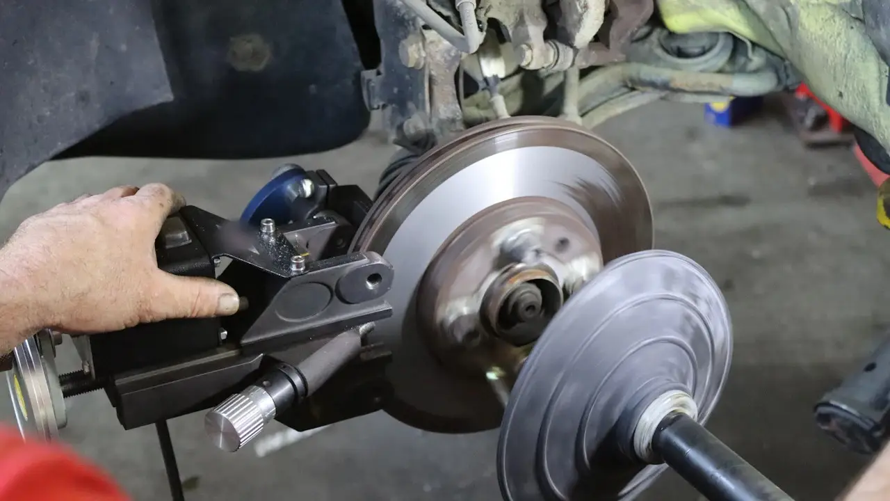 A mechanic's hand on an on-car brake lathe beside a brake rotor, the wheel removed.