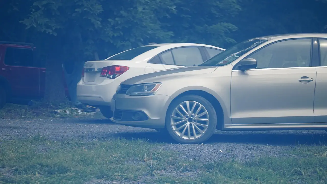 Two sedans parked on a gravel lot beside trees.