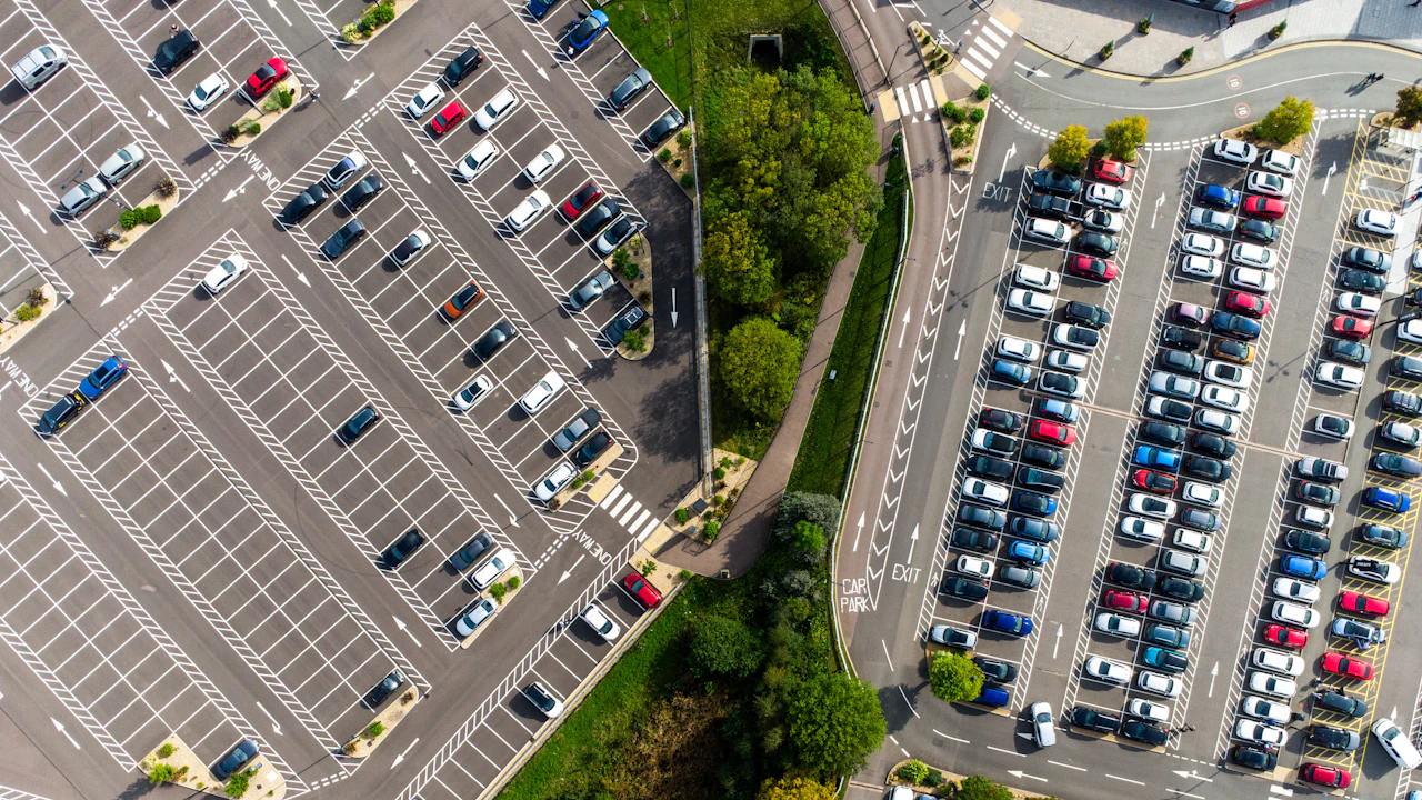 An aerial view of two large car parks with rows of parked cars on either side of a tree-lined road.