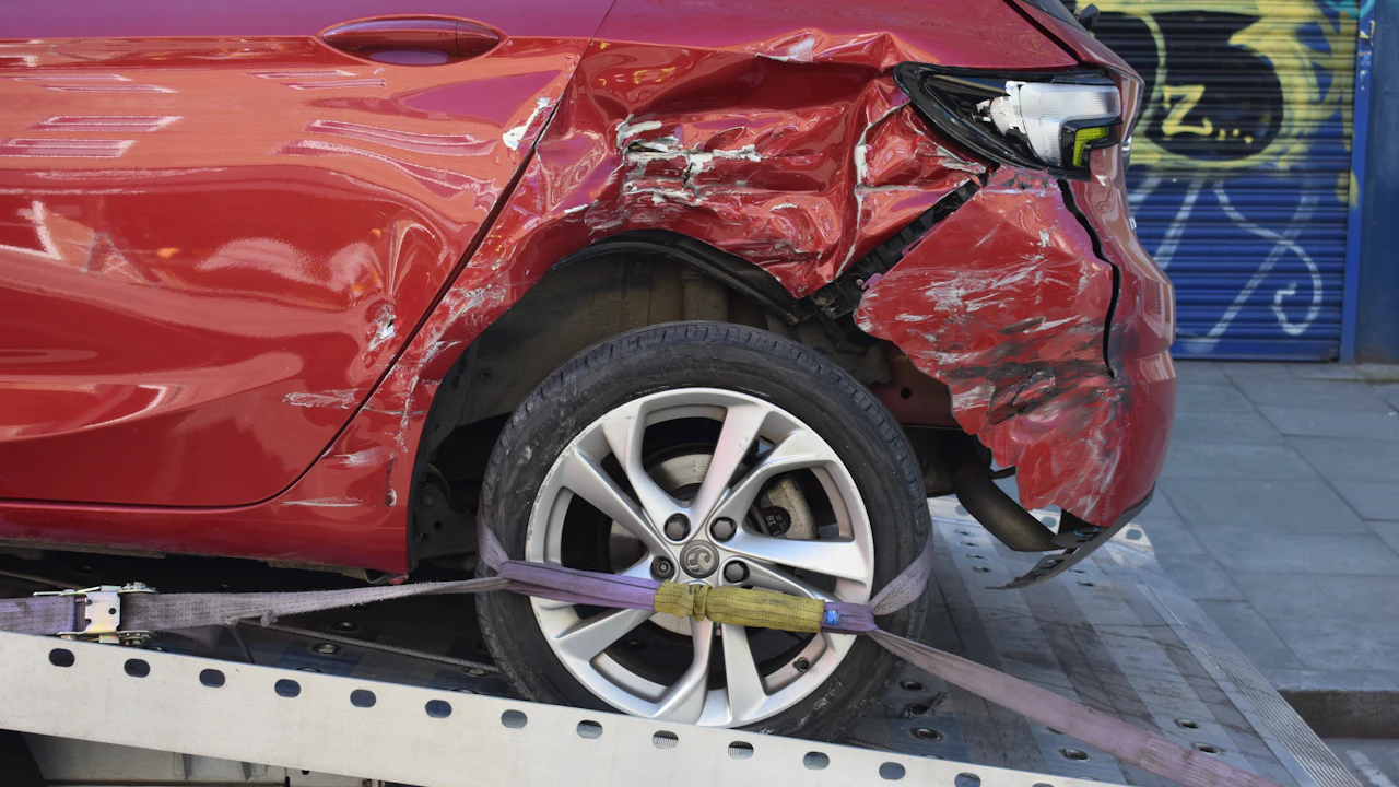 A red hatchback with severe rear-quarter collision damage strapped to a flatbed recovery truck