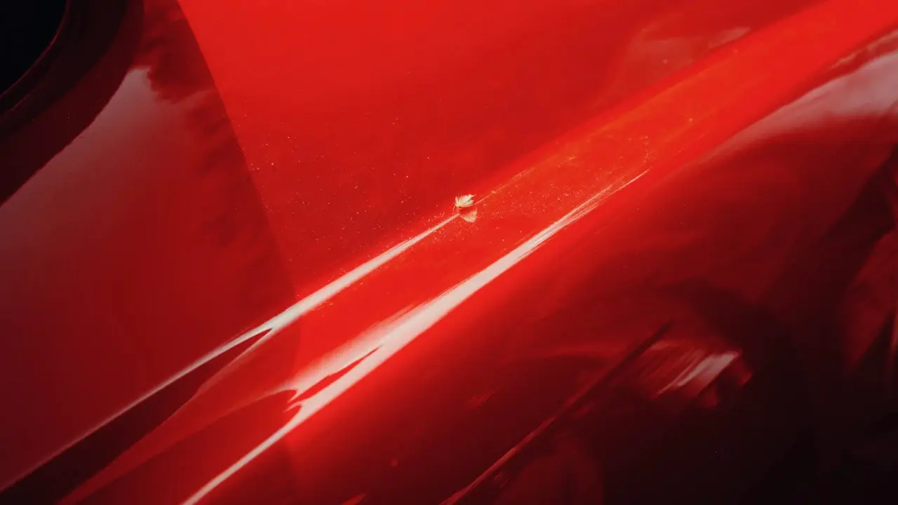 Close view of a scratch and chip in a red car's paint.