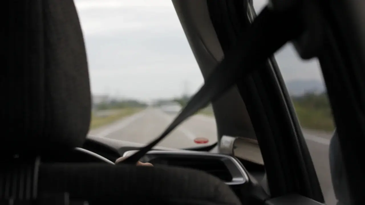 A car's front seat belt, with the road ahead through the windscreen.
