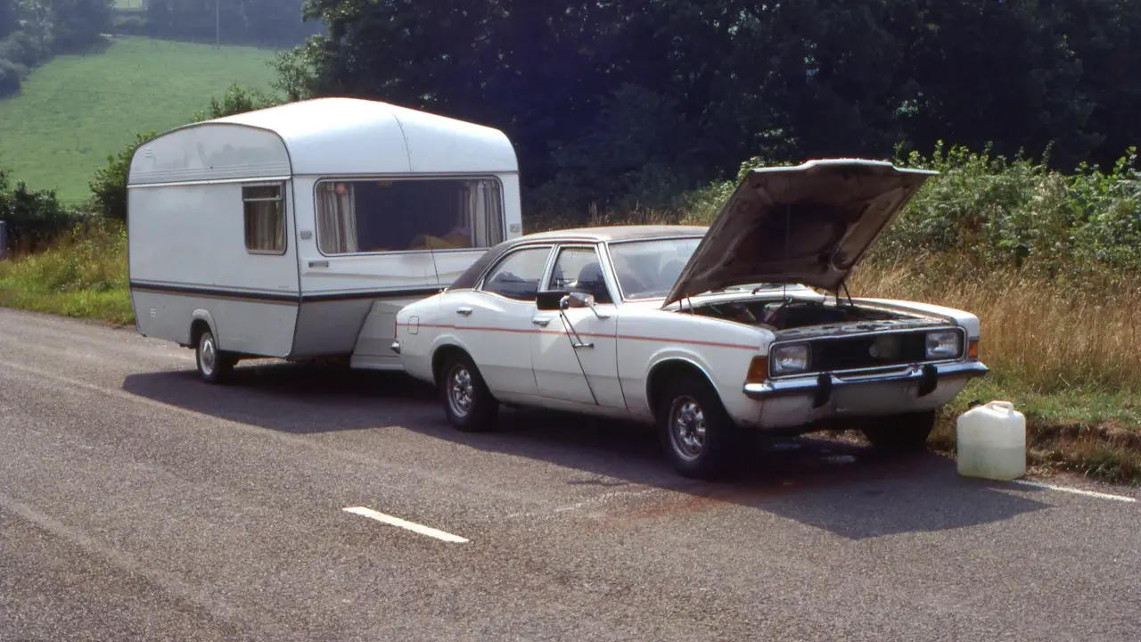 An older sedan parked by a country road with its hood open.