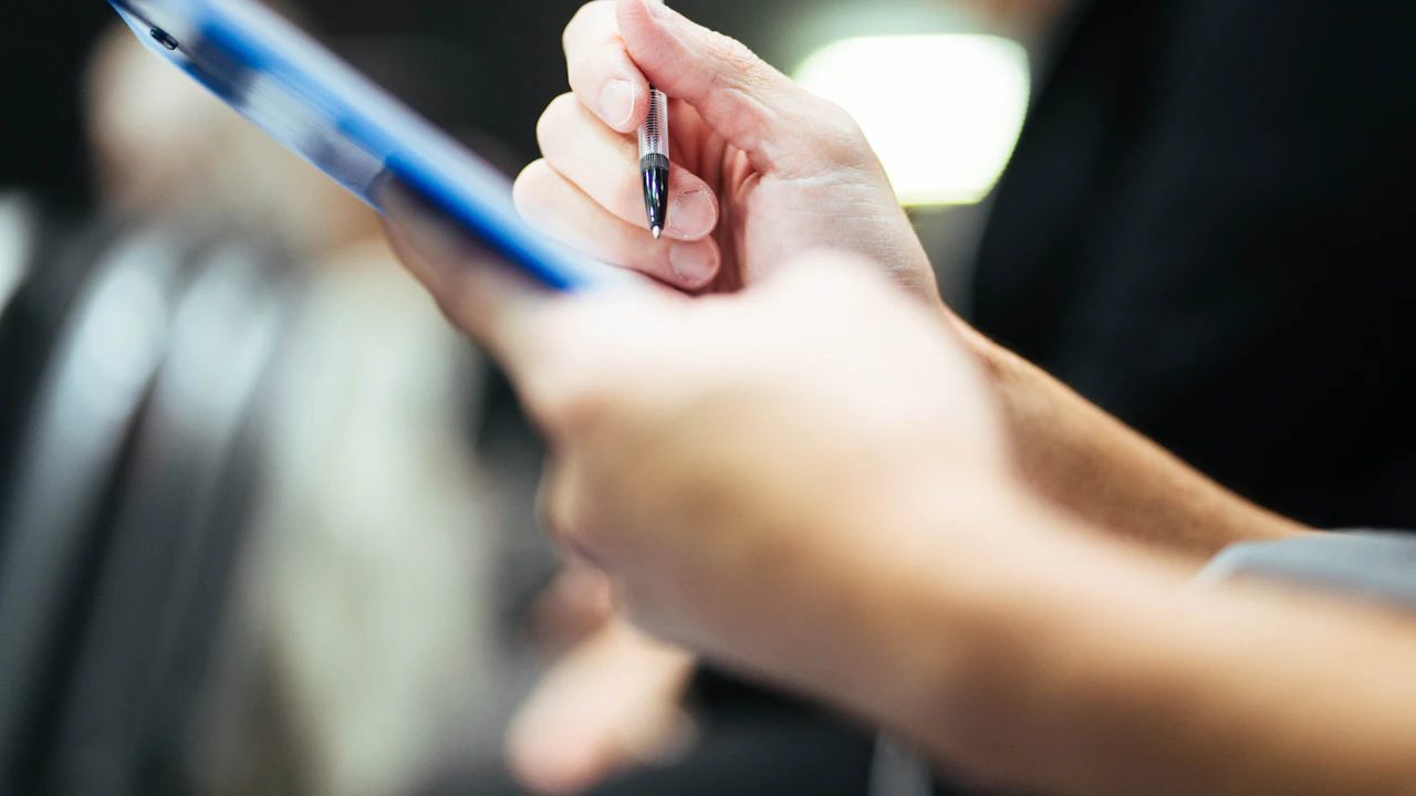 A close-up of a person holding a clipboard and pen, about to write up a job