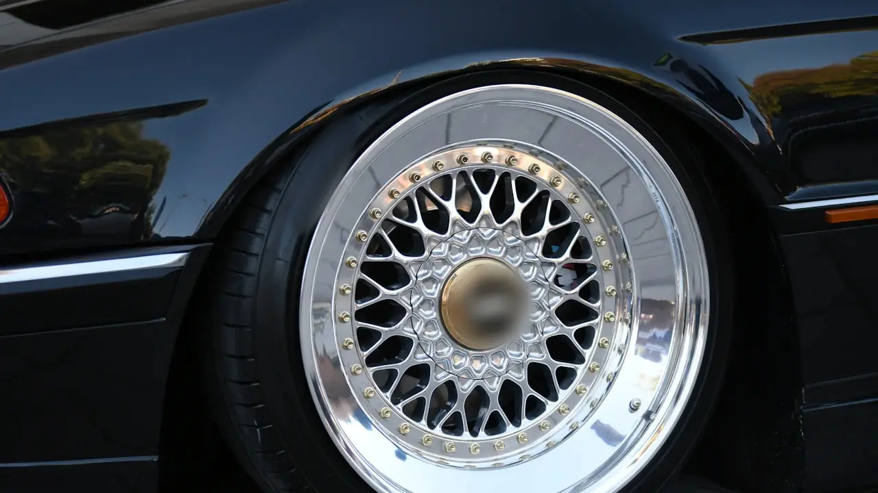 A polished multi-spoke wheel and the tire around it on a black car.