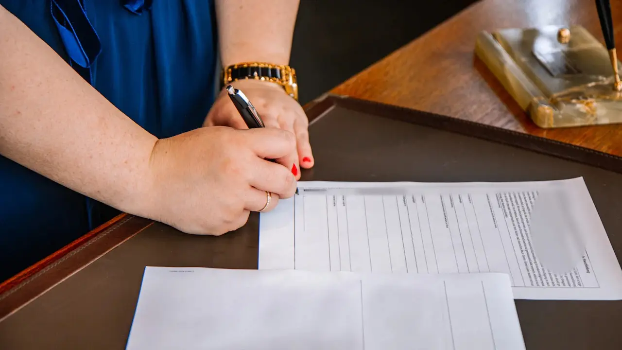 A hand signing a printed form on a desk with a pen.