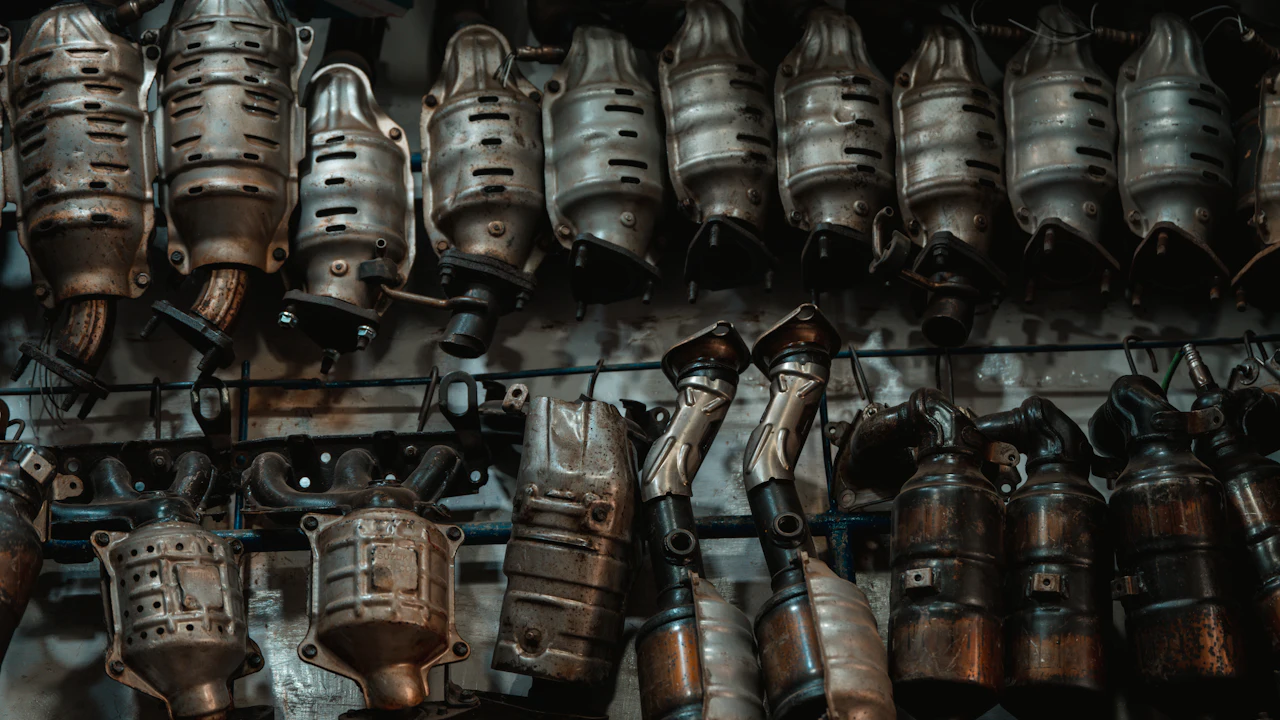 Rows of used catalytic converters and exhaust manifolds hanging on a workshop wall