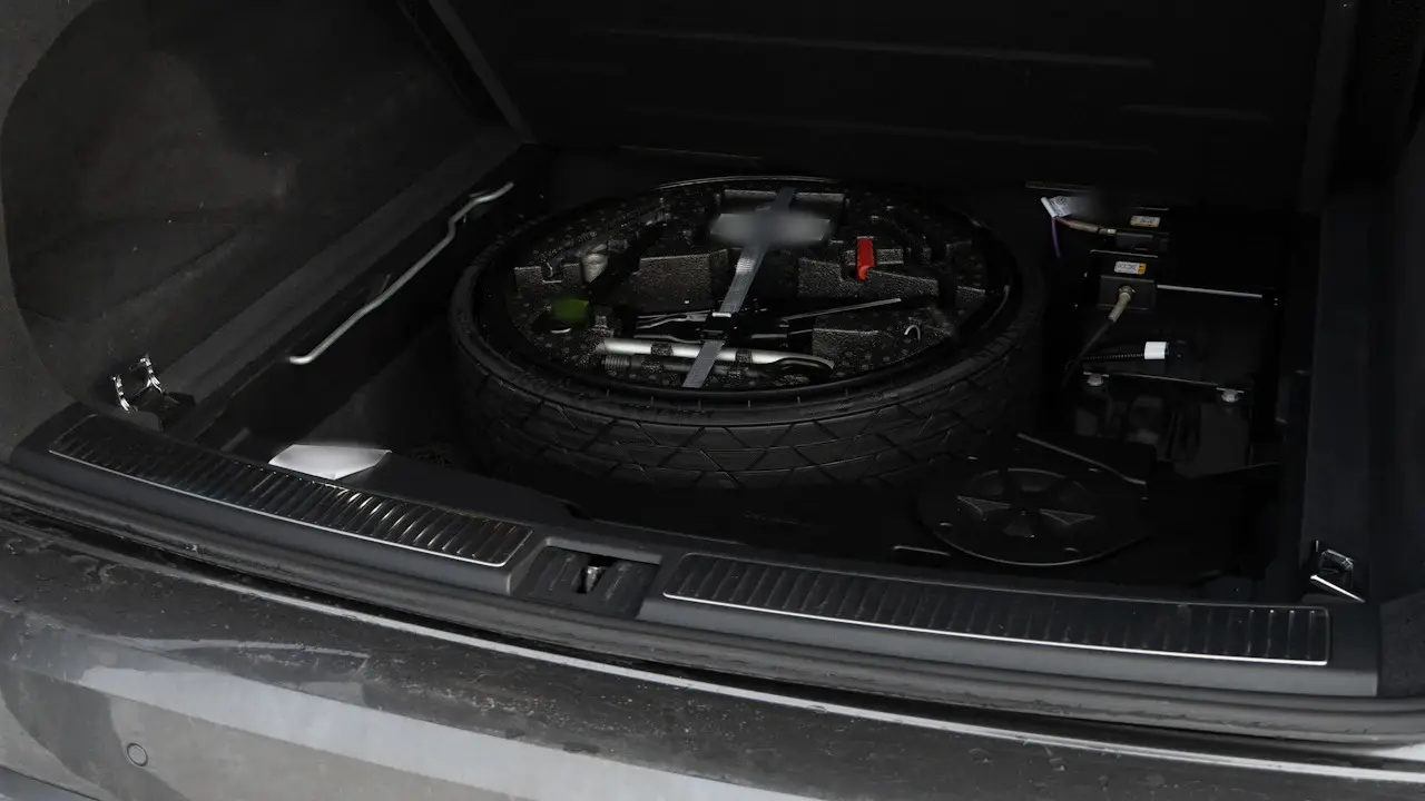 A spare tire and its tools stored under a car’s trunk floor.