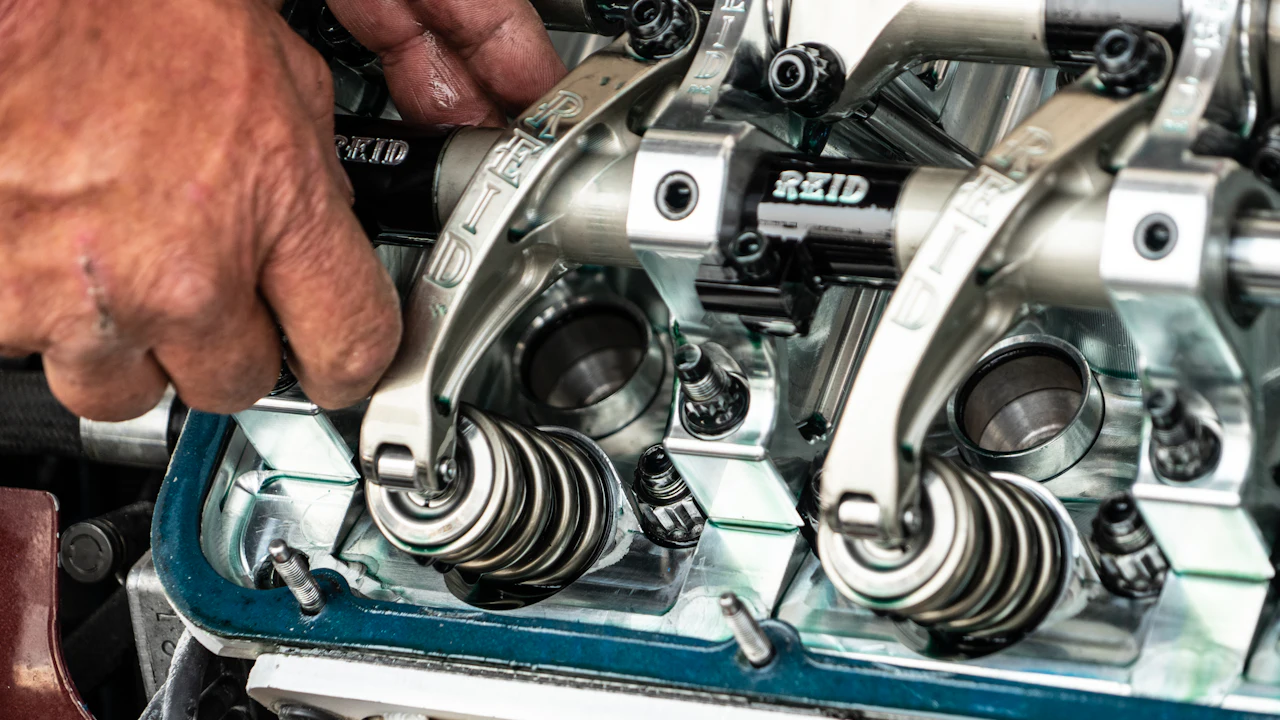 A cylinder head with its cover removed, valve springs visible, a hand reaching in to work on it